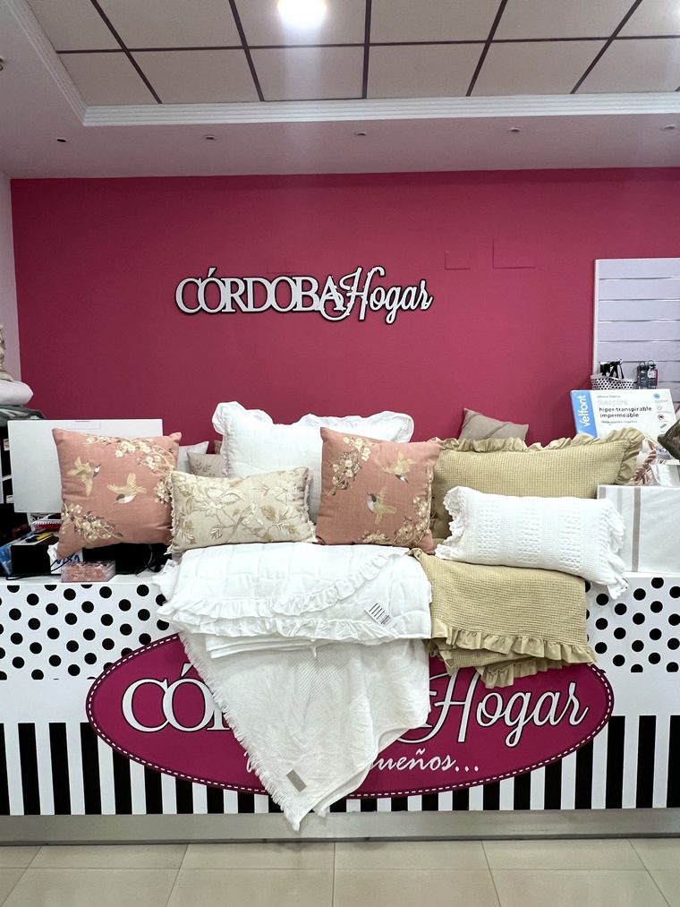 Expositor de la tienda con un conjunto de colcha y cojines a juego bajo el logo de Córdoba Hogar