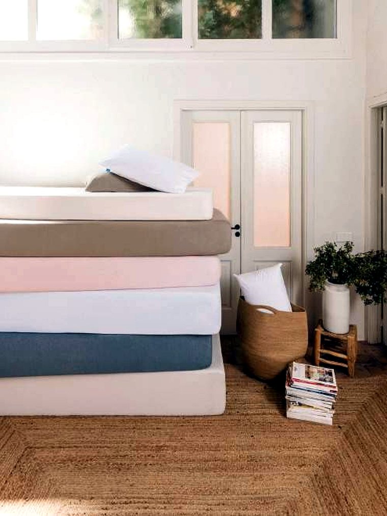 Pila de protectores y bajeras en tonos neutros y rosa sobre un colchón